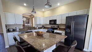 A modern kitchen with white cabinets, a granite island, stainless steel appliances, and pendant lighting. - Lakeside at Lake Berkley close to Disney (Kissimmee)