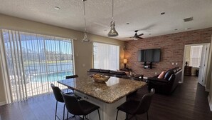 A spacious kitchen with a central island, bar stools, a dining area, a fireplace, and a large window overlooking a pool. - Lakeside at Lake Berkley close to Disney (Kissimmee)