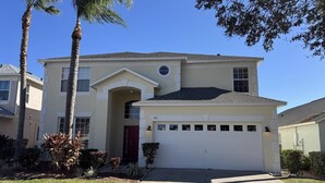 A two-story house with a garage, palm trees, and a well-maintained lawn. - Lakeside at Lake Berkley close to Disney (Kissimmee)