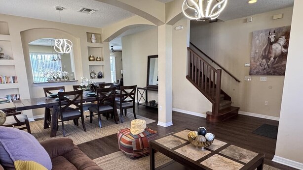 A spacious living room with a brown couch, a dining area with a wooden table and chairs, a staircase, and a large painting on the wall. - Lakeside at Lake Berkley close to Disney (Kissimmee)