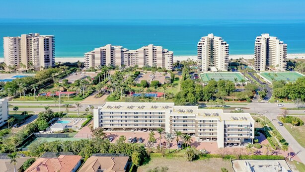 A high-rise hotel complex with multiple buildings, a swimming pool, tennis courts, and a beach view.