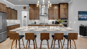 A modern kitchen with wooden cabinets, a central island with bar stools, stainless steel appliances, and a chandelier. - Cadillac on the Colorado | Concierge Services (Kingsland)