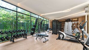 A gym with weightlifting equipment, cardio machines, and large windows offering a view of greenery. - One block from beach in Hotel Zone-Free Beach Club (Tulum)