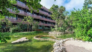 A multi-story building with balconies, surrounded by a landscaped garden with a pond and stone pathways. - One block from beach in Hotel Zone-Free Beach Club (Tulum)