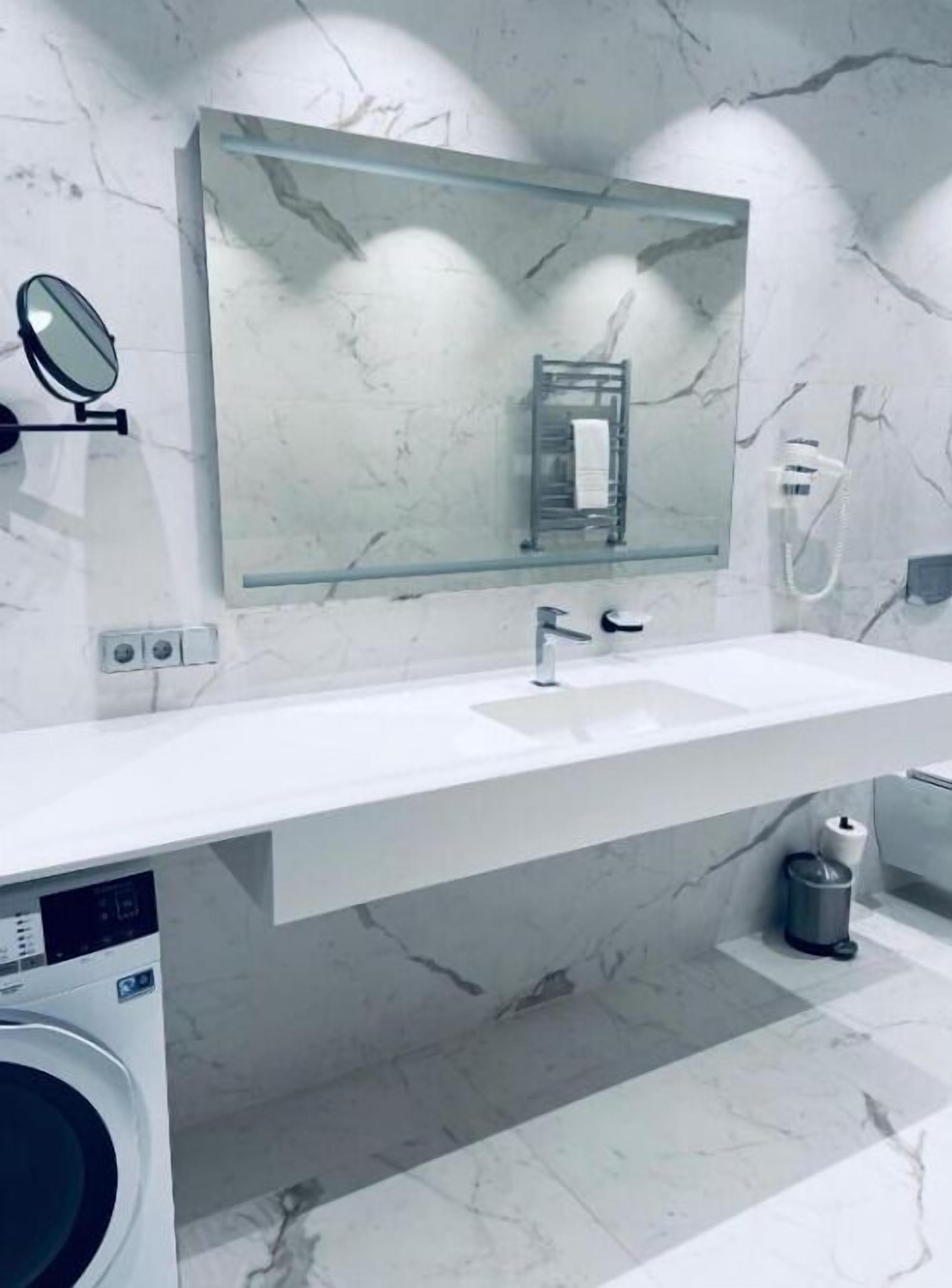 A modern bathroom with a marble backsplash, a glass mirror, a sink, and a washing machine.