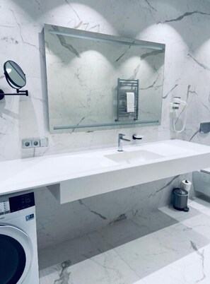 Un baño moderno con un salpicadero de mármol, un espejo de cristal, un lavamanos y una lavadora.