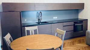 A modern kitchen with a round wooden table and four chairs, a built-in oven, and a dark-colored backsplash.