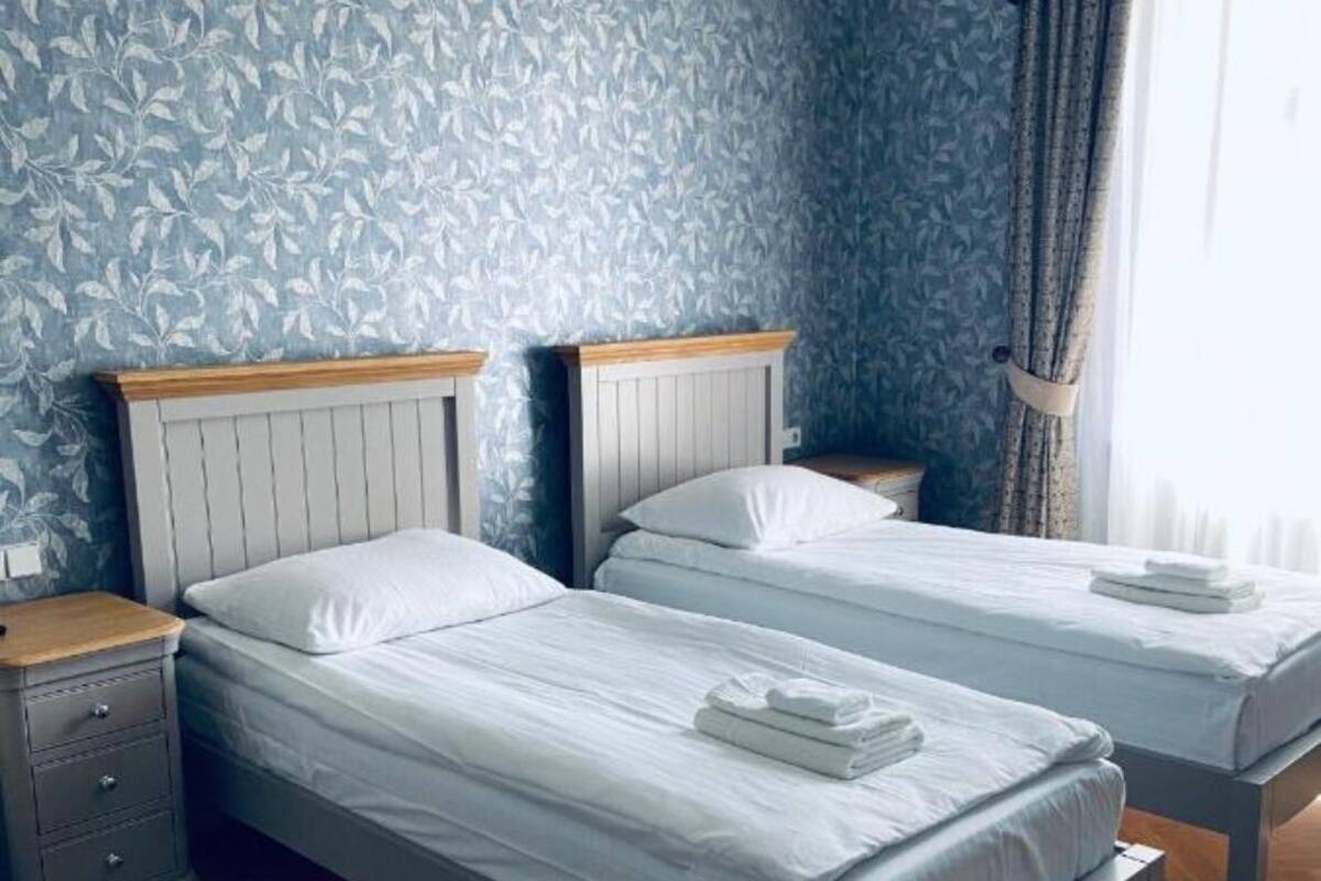 A room with two beds, wooden headboards, a nightstand, and a window with curtains.
