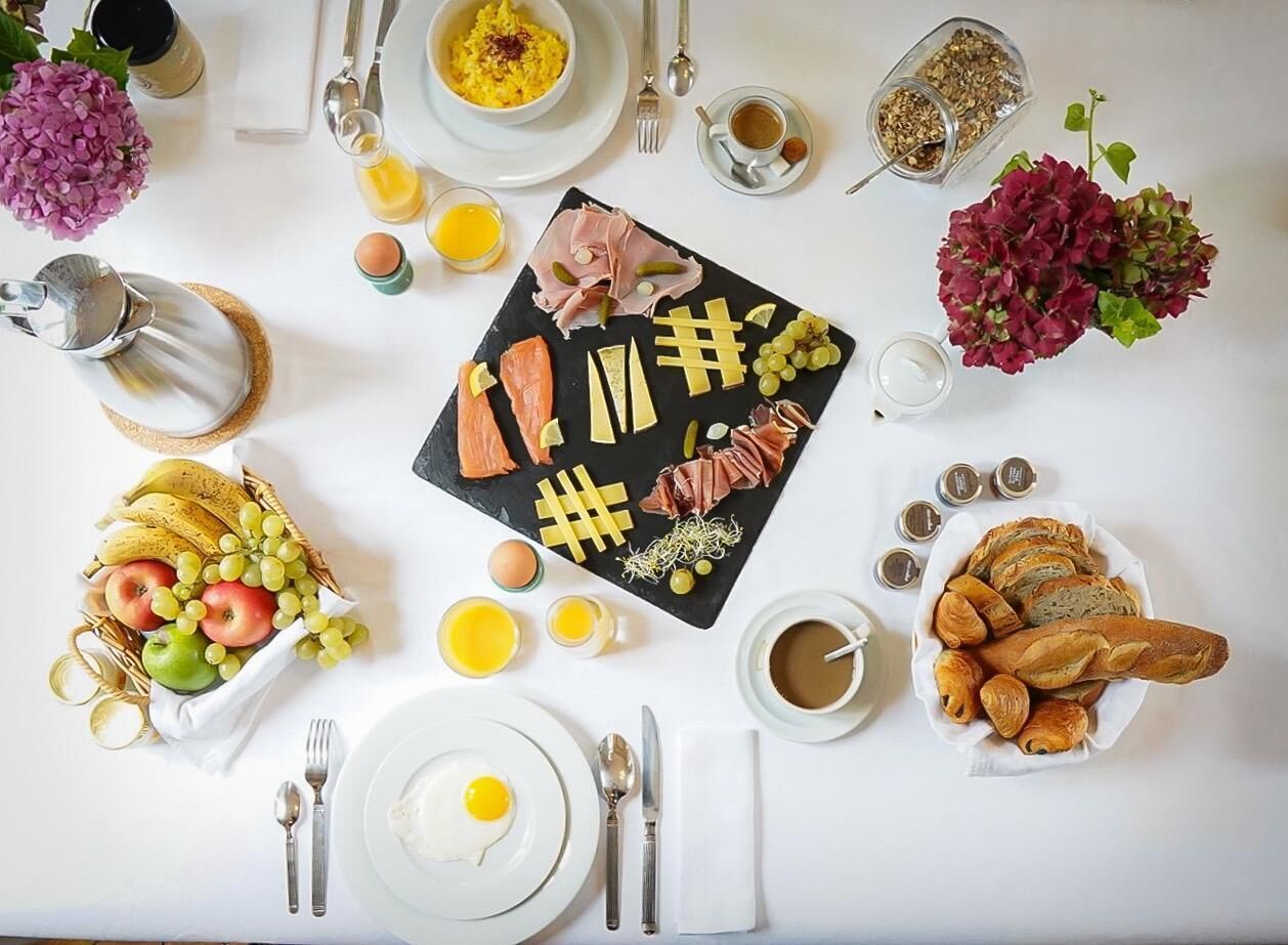 A breakfast setting with a variety of foods including eggs, meats, cheese, and fruits, arranged on a white table with a black slate board.