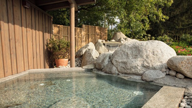 A clear pool with a wooden deck, surrounded by rocks and a wooden fence.