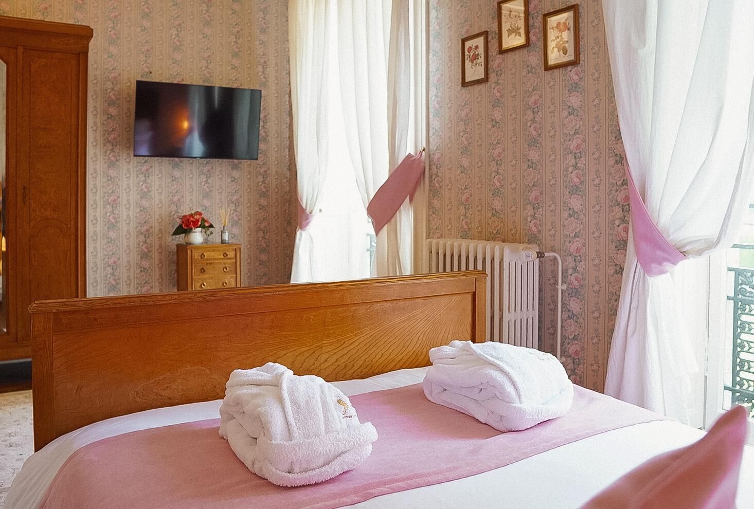 Habitación de hotel con una cama de madera, dos toallas, un televisor, papel tapiz floral y un radiador.