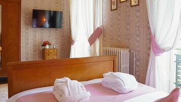 Habitación de hotel con una cama de madera, dos toallas, un televisor, papel tapiz floral y un radiador.