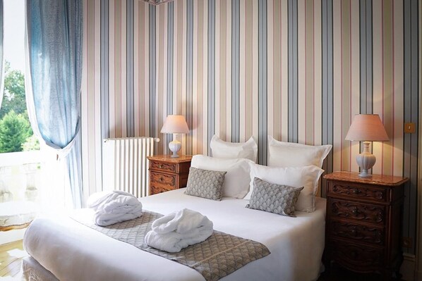 Habitación de hotel con una cama grande, dos mesitas de noche con lámparas, una ventana con cortinas y vistas a zonas verdes.
