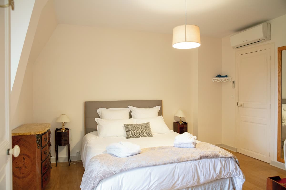 A bedroom with a bed, bedside tables, a dresser, and an air conditioning unit.