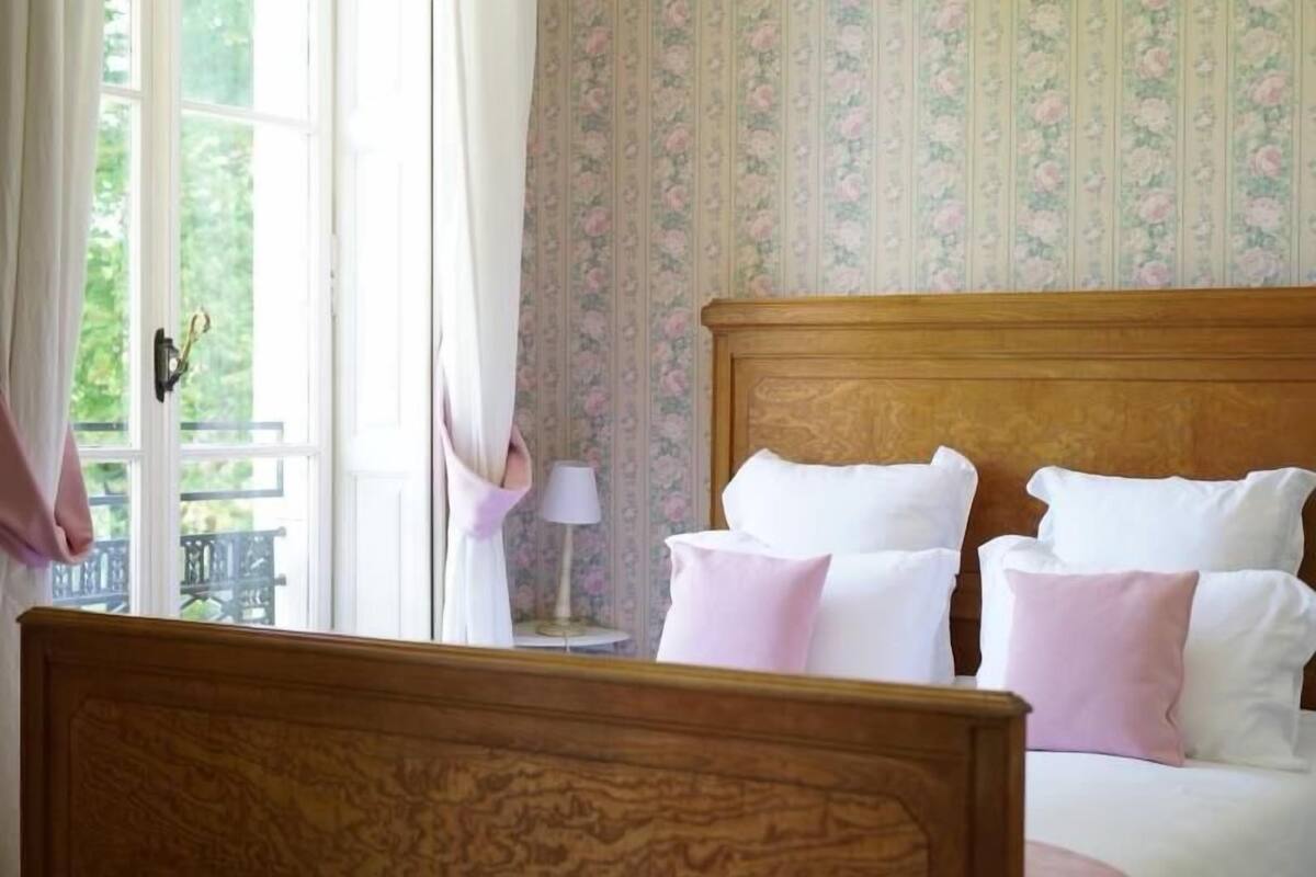 A bedroom with a wooden headboard, white bedding, and a floral wallpaper pattern.