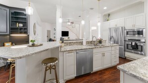A modern kitchen with white cabinetry, granite countertops, stainless steel appliances, and pendant lighting.