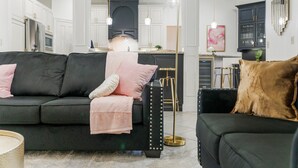 A modern living room with a black sofa, a gold floor lamp, and a kitchen in the background.