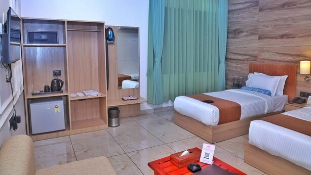 A hotel room with a bed, a desk, a wardrobe, a mini-fridge, and a ceiling fan. - Hotel Lotus (Botad)