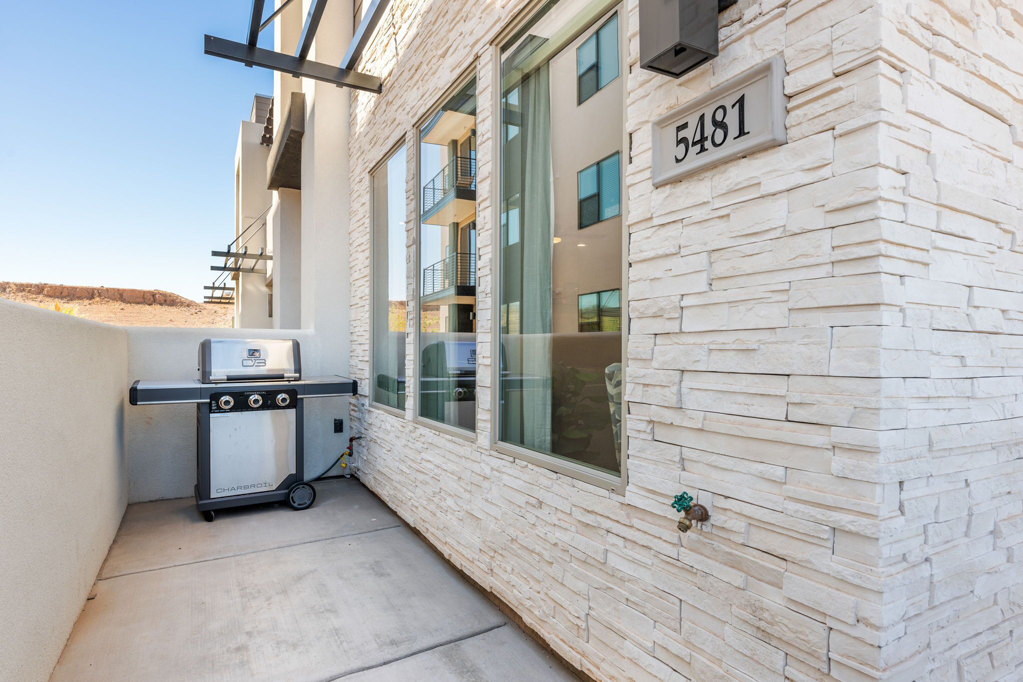A modern building with a stone facade, a visible number 5481, and a barbecue grill outside.
