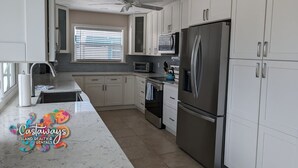 A modern kitchen with white cabinets, a stainless steel refrigerator, a microwave, and a ceiling fan. - Dream Vacation Pool and Waterfront Location (Saint James City)