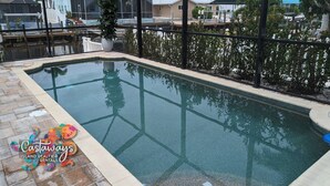 A rectangular swimming pool with clear water, surrounded by a tiled deck and a glass enclosure. - Dream Vacation Pool and Waterfront Location (Saint James City)