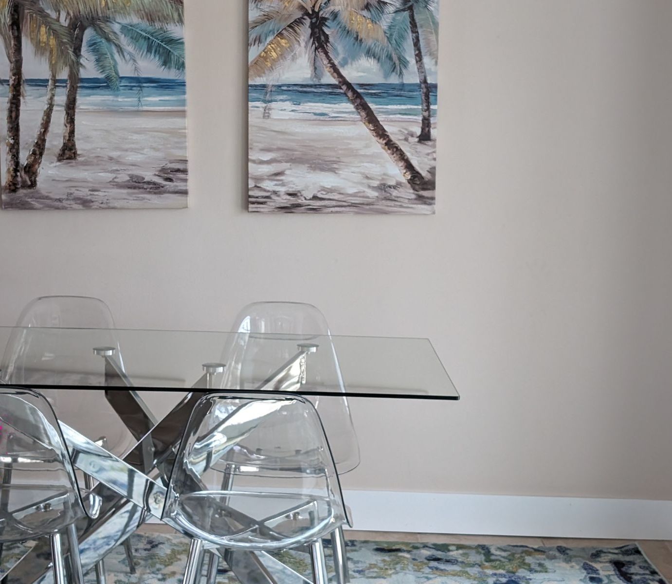 A dining area with a glass table and four chairs, two paintings of a beach scene on the wall, and a logo for Castaways Island Realty & Rentals.