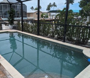 Une piscine rectangulaire à l’eau claire, entourée d’une terrasse carrelée et protégée par une paroi de verre.