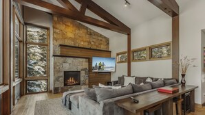 A modern living room with a stone fireplace, large windows, a grey sofa, and a wooden ceiling. - New Modern Chalet by InvitedHome | Shuttle to Ski, Lounges, Deck, Firepit, Views (Breckenridge)
