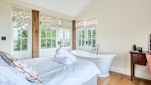 Une chambre à coucher avec un grand lit, une baignoire blanche et un bureau en bois.