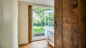 Une pièce avec une porte en bois, un mur blanc et une vue sur un jardin, visible à travers une porte vitrée.