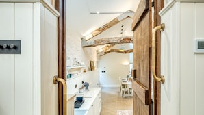 Un couloir étroit, avec une porte en bois rustique et une cuisine moderne visible au fond.