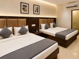 A hotel room with two beds, a wooden headboard, a wall-mounted air conditioner, and a framed picture above the beds.