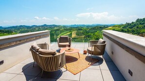 Eine Terrasse mit Korbmöbeln, einem Tisch mit Flasche und Gläsern sowie Blick auf Weinberge.