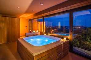 A modern bathroom with a hot tub, large windows, and a view of the city at night.