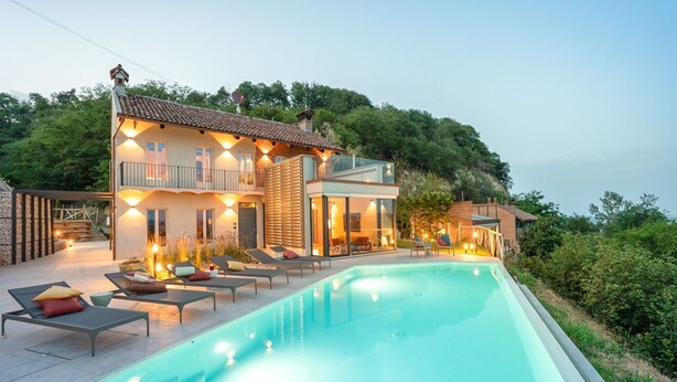 Eine moderne Villa mit Swimmingpool, Sitzgelegenheiten im Freien und Blick auf die umliegende Grünfläche.
