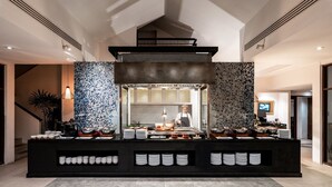 A buffet area with a chef preparing food, surrounded by a black counter with white plates and bowls. - Dewa Phuket - Deluxe Garden (Sa Khu)