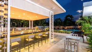 An outdoor bar area with a pool in the background, surrounded by lounge chairs and palm trees. - Dewa Phuket - Deluxe Garden (Sa Khu)