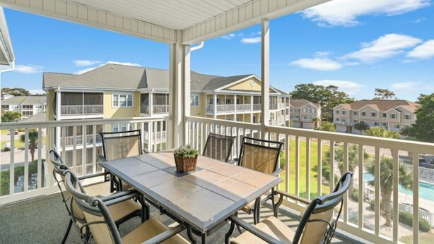 A covered outdoor patio with a table and chairs, overlooking a residential area with multiple houses. - Ocean Keyes 2242- 2BR/2BA-Close to Main St (North Myrtle Beach)