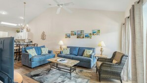 A spacious living room with a blue sofa set, a coffee table, a wicker armchair, and a ceiling fan. - Ocean Keyes 2242- 2BR/2BA-Close to Main St (North Myrtle Beach)