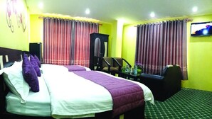 A hotel room with a bed, two chairs, a TV, and curtains.