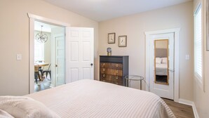 A bedroom with a bed, a dresser, a door, and a small table.