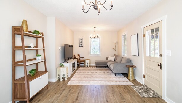 A spacious living room with a wooden floor, a grey sofa, a TV, and a chandelier.
