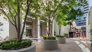 A modern outdoor area with large planters, trees, and a building with a glass facade. - Luxury and Spacious City Views Pool, Gym & Sauna (Buenos Aires)
