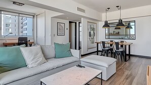 A modern living room with a sofa, a coffee table, and a dining area with chairs and a table. - Luxury and Spacious City Views Pool, Gym & Sauna (Buenos Aires)