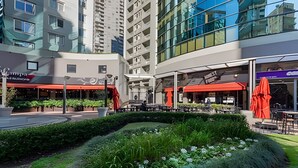 Une cour intérieure urbaine moderne, dotée d’un espace de détente en plein air, d’un jardin aménagé et, en arrière-plan, de bâtiments de grande hauteur.