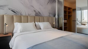 Une chambre à coucher moderne avec un grand lit, une tête de lit, des lampes de chevet, une armoire et un miroir.