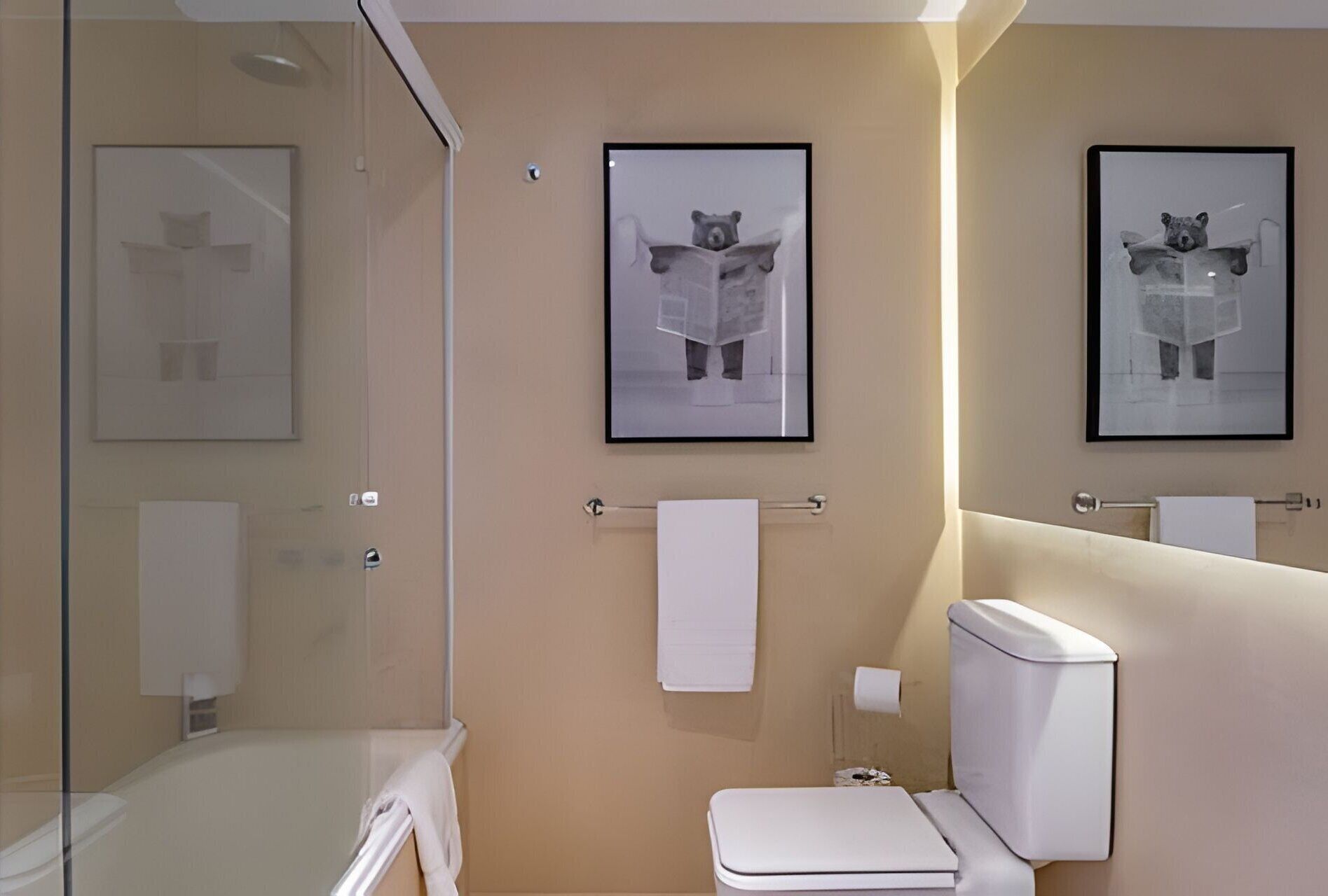 Un baño moderno con cabina de ducha de vidrio, un inodoro y dos cuadros enmarcados con imágenes de un oso.