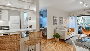 Un salon moderne comprenant un canapé, des fauteuils, un coin repas et une cuisine visible à travers une porte ouverte.