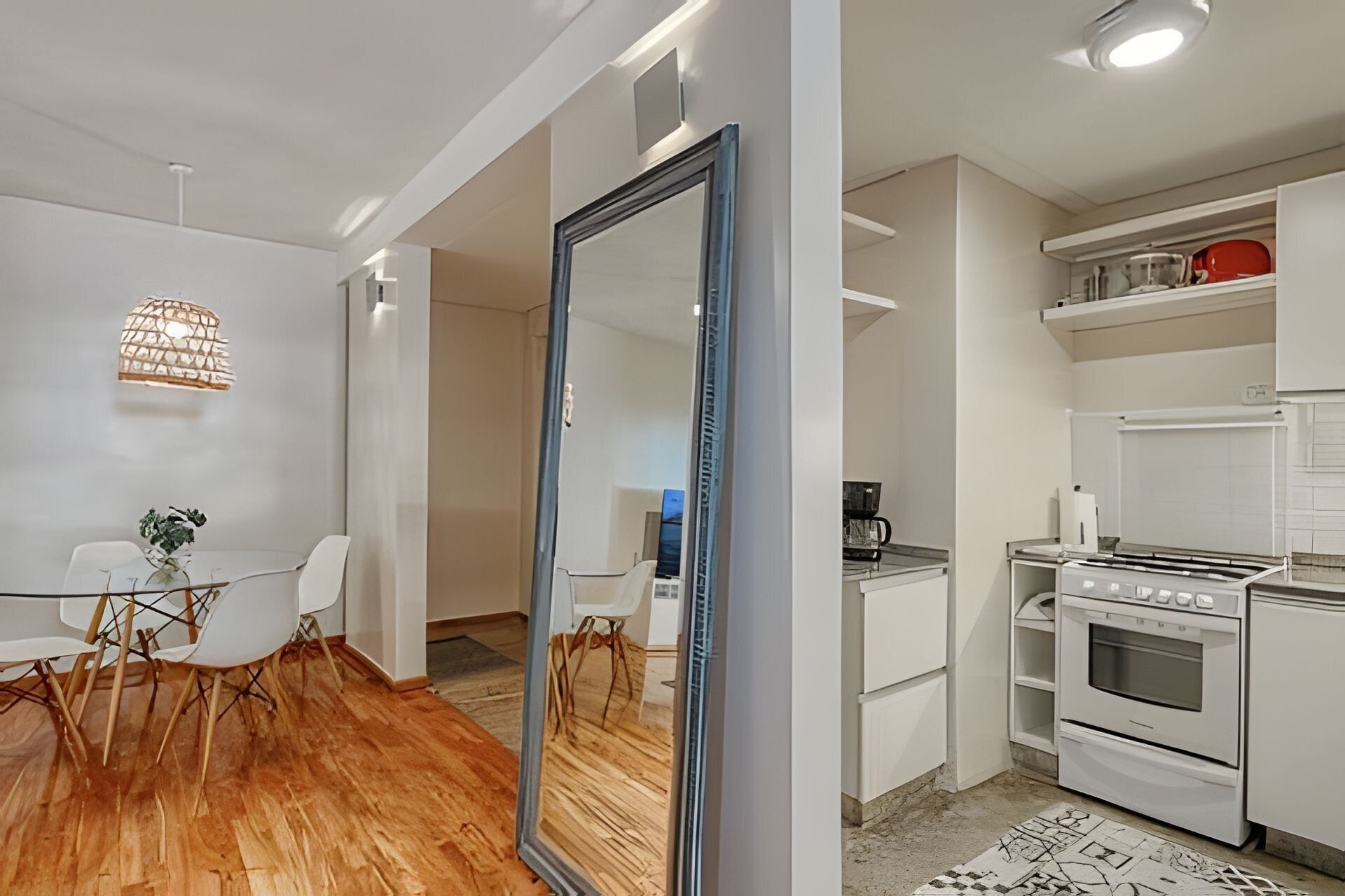 Une cuisine moderne avec des appareils électroménagers blancs, un coin repas avec une table et des chaises en verre, et un grand miroir.