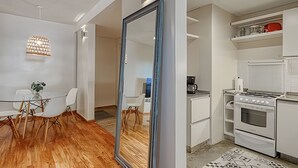 Une cuisine moderne avec des appareils électroménagers blancs, un coin repas avec une table et des chaises en verre, et un grand miroir.